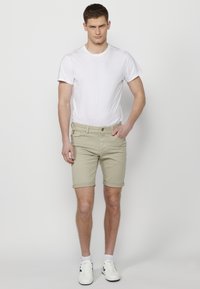 Pantalones cortos de color beige claro con dobladillos enrollados, combinados con una camiseta blanca ajustada y calzado blanco. Sin patrones visibles ni detalles de hardware.