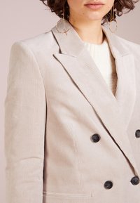 Beige Corduroy-Doppelkinnblazer mit Revers, ausgestattet mit dunklen Knöpfen und einer feinen Rippstruktur.