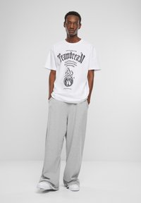 Hvid t-shirt med sort grafisk tekst og flammedesign, parret med løse grå sweatpants. Canvastøvler fuldender outfittet.