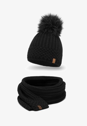 Schwarze gestrickte Mütze mit einem Fellpompon und einem passenden schwarzen gestrickten Schal. Beide haben ein strukturiertes Muster und ein kleines Leder-Logoetikett.