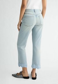 Jeans cropped in denim azzurro con bordo in pizzo floreale, dotati di due tasche posteriori e una vestibilità dritta. Scarpe decorate in nero e argento.