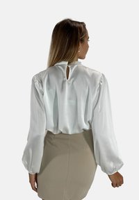 Witte satijnen blouse met pofmouwen en een keyhole-achterkant, gecombineerd met een beige aansluitende rok. Soepele textuur en vloeiende ontwerp.