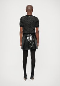 Top corto nero con un motivo logo sottile; abbinato a una mini gonna in vinile nera lucida a vita alta; collant neri e tacchi completano il look.