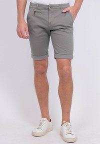 Shorts en coton gris avec des poignets roulés, dotés d'une poche latérale avec un accent en cuir, portés avec des baskets blanches à lacets.