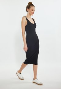 Abito midi nero a coste con scollo a V e spalline sottili, abbinato a sneakers bianche con suola in gomma. Design semplice, silhouette attillata.