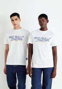 Balti medvilniniai marškiniai trumpomis rankovėmis su "RED BULL RACING" logotipu mėlyna ir geltona spalvomis. Unisex dizainas, derinamas su mėlynomis džinsomis.