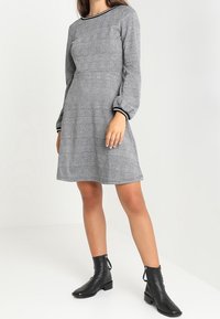 Grå mönstrad klänning med långa puffärmar, rundad halsringning och svart kant, i kombination med svarta ankelskor. Slät textur.