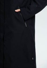 Giacca impermeabile nera con tasca con zip e design elegante. Il materiale appare liscio con una finitura opaca e hardware minimale.