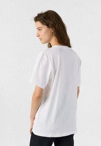 Camiseta blanca de algodón con un corte relajado, mangas cortas y cuello redondo. La tela parece suave, con bordes limpios y sin patrones visibles.
