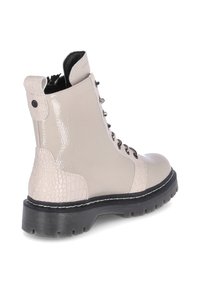 Beige kotníkové boty s lesklým povrchem a texturovanými krokodýlími akcenty, šněrovací přední část a silná černá gumová podrážka s bílými stehy.