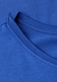 Gros plan sur l'encolure d'un T-shirt en coton bleu, montrant une couture côtelée fine et une texture de tissu lisse.