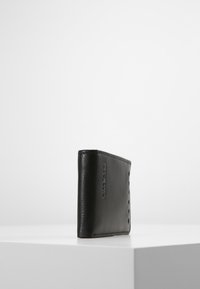 Portafoglio in pelle nera con una texture liscia, design minimalista e dettagli cuciti lungo i bordi. Forma rettangolare compatta.