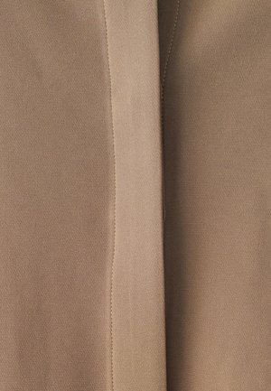 Beige stof met een gladde textuur, met gestikte naden en subtiele variaties in tint, gevouwen om zijn zachte val te tonen.