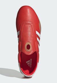 Crvene kožne tenisice s bijelim prugama, zaobljenim vrhom i bež kružnim naglaskom na vrhu. Imaju unutrašnji dizajn s podstavom.