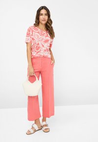 Kurzarmpullover in Koralle mit weißem Blumenmuster, kombiniert mit weiten Hosen in Koralle, einer weißen Handtasche und Sandalen mit silberner Schnalle.