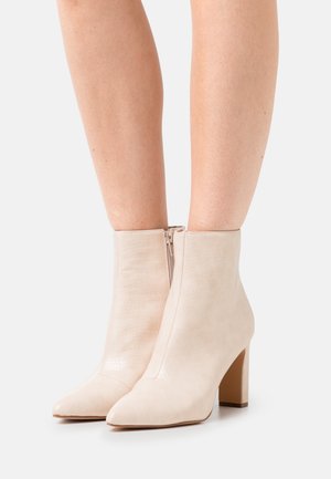 Bottines beiges en cuir texturé, bout pointu et fermeture éclair latérale. Dotées d'un talon moyen carré pour une meilleure stabilité.