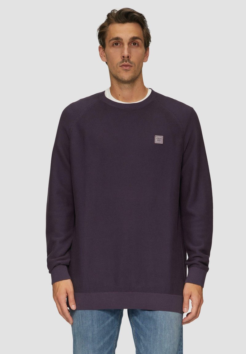 Lila Sweatshirt mit gerippter Textur, Rundhalsausschnitt und langen Ärmeln. Mit einem kleinen Logo-Patch auf der linken Brust und hüftlang geschnitten.