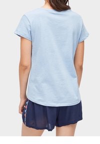 Ljusblå bomulls t-shirt med korta ärmar, rund halsringning och slät textur, kombinerad med marinblå shorts med geometriskt mönster.