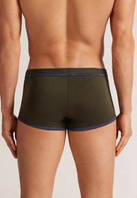 Zelené boxerky s modrými páskovými akcenty, přiléhavý design a hladká textura, zobrazující zadní pohled na neutrálním pozadí.