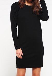 Abito nero a maniche lunghe dal design aderente, realizzato in materiale morbido, con scollo rotondo e orlo appena sopra il ginocchio.