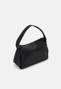 Borsa nera con una texture liscia e morbida, forma trapezoidale e una tracolla larga con marchiatura in rilievo. Chiusura superiore con zip.