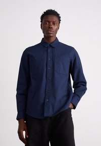 Camicia button-up blu scuro con colletto classico, due tasche sul petto e maniche lunghe con polsini abbottonati, realizzata in un tessuto morbido.