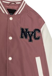 Veste bomber rose avec manches blanches, boutons pression blancs et logo brodé "NYC" en marine. Dotée d'un col rayé et d'une texture lisse.