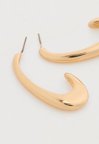 Σκουλαρίκια από μέταλλο σε χρυσό τόνο με ομαλή, κυρτή σχεδίαση, που έχει μυτερό άκρο και καρφί για στερέωση. Η υφή της επιφάνειας αντανακλά το φως.