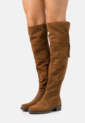 Bottes en suède marron au-dessus du genou avec un design loose et un talon plat. Présente une couture subtile et une fermeture à glissière.