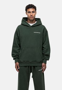 Felpa con cappuccio verde scuro realizzata in morbido tessuto, con tasca frontale e scritta bianca "GOODFORNOTHING" sul petto. Vestibilità casual e rilassata.