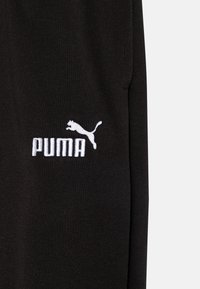 Tissu noir au toucher lisse, avec un logo "PUMA" brodé en blanc et une silhouette de puma en saut sur le côté gauche.