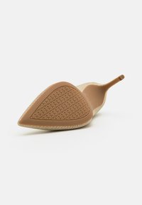 Beige korkokengät, joissa on teksturoitu, terävä kärki ja suloinen muotoilu. Pohjassa on kuvioitu pito, joka tarjoaa vakautta.