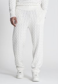 Witte gebreide joggingsbroek met een gestructureerd kabelpatroon, geribbelde tailleband en boorden. Gepaard met witte sneakers.