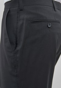 Pantalon noir au design épuré, avec des poches latérales, une poche arrière avec fermeture à bouton et une texture lisse.