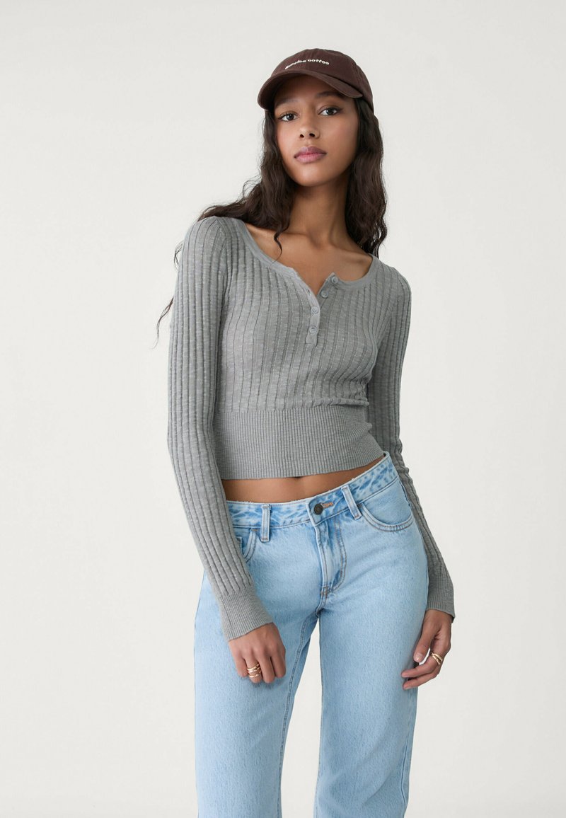 Gray ribbed cropped sweater with long sleeves and button detail, paired with light blue high-waisted jeans.