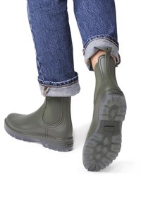 Roheline kummist pahklu وتصboots elasti külgede paneelidega, tekstureeritud tallad ja logo detail kontsakul, koos rullitud teksadega.