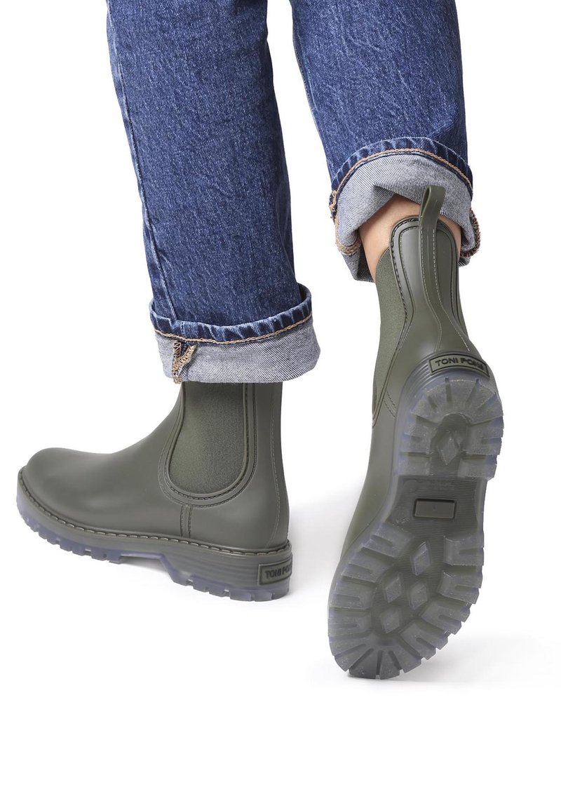 Roheline kummist pahklu وتصboots elasti külgede paneelidega, tekstureeritud tallad ja logo detail kontsakul, koos rullitud teksadega.