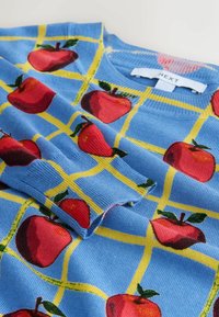 Blue knitted sweater featuring red apples on a yellow grid pattern, with a crew neck and ribbed cuffs. Label located at the neckline.