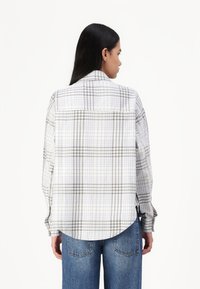 Camisa de algodão de manga longa em padrão xadrez cinza e branco, com bainha arredondada e punhos abotoados, combinada com jeans denim azuis.