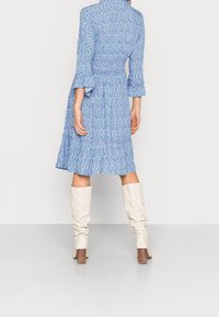 Modré květinové šaty s dlouhými rukávy, sytým pasem a volánovým lemem, doplněné krémovými kozačkami nad kolena a hnědými botami na blokovém podpatku.