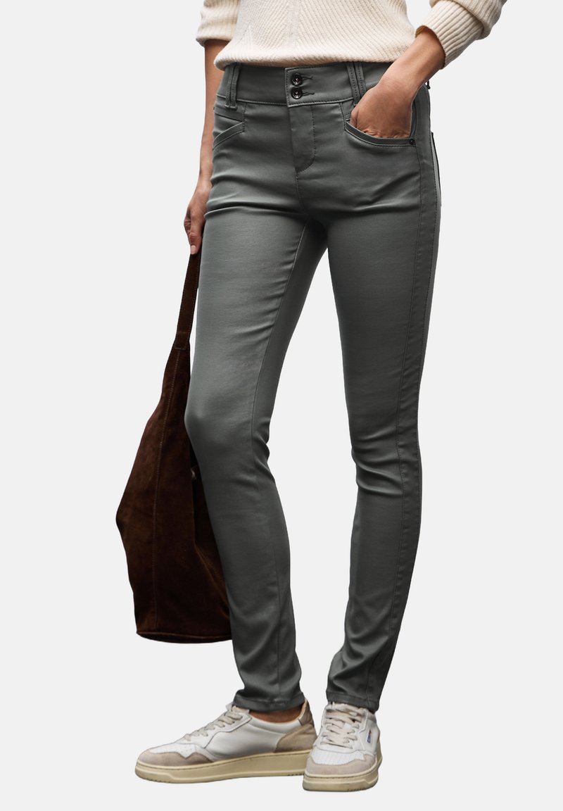 Grå tightsbyxor med en mjuk textur, två framfickor och knäppning. Bärs med vita sneakers och en brun väska.