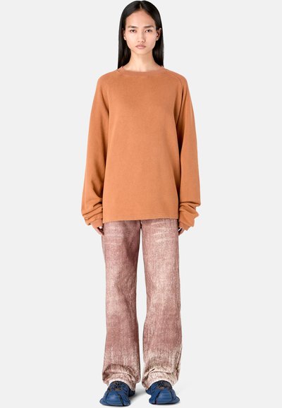 Oversized terracotta sweater, textured material; paired with pink-toned, distressed wide-leg pants and blue sporty footwear.