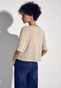 Beiger strukturierter Strick-Top mit weitem Rundhalsausschnitt und kurzen Ärmeln, kombiniert mit dunkelblauen Jeans, seitlich-hinten betrachtet.