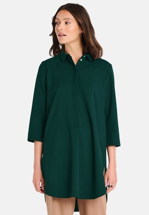 Dark green, button-up tunic shirt with a collar, ¾ sleeves, and side slits. Made of a smooth fabric with a relaxed fit.