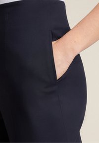 Marinblå byxor i slätt tyg med sid ficka. Har rena linjer och en skräddarsydd passform. Utmärker sig för sin minimalistiska design.