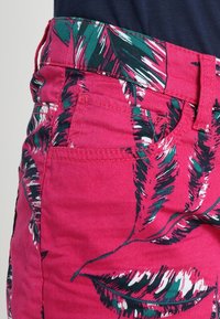 Pink shorts with a tropical leaf print in green and white. Features a waistband, pockets, and contrasting stitching. Made of cotton fabric.