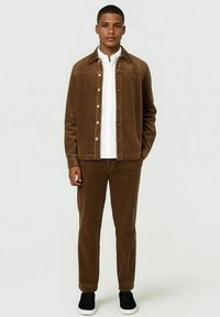 Brown corduroy jas en bijpassende broek, met een wit shirt eronder. De jas heeft een knoopsluiting en een zachte textuur.