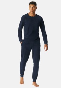 Mørkeblå loungewear sæt lavet af blødt stof, der har ribbet tekstur, lange ærmer og tætsiddende joggerbukser med elastiske manchetter.