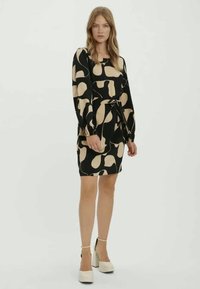 Μαύρο φόρεμα με μπεζ αφηρημένα σχήματα, μακριά μανίκια, εφαρμοστό μέση και ζώνη με κόμπο; λεία ύφανση, μήκος πάνω από το γόνατο, φορεμένο με πλατφόρμες.