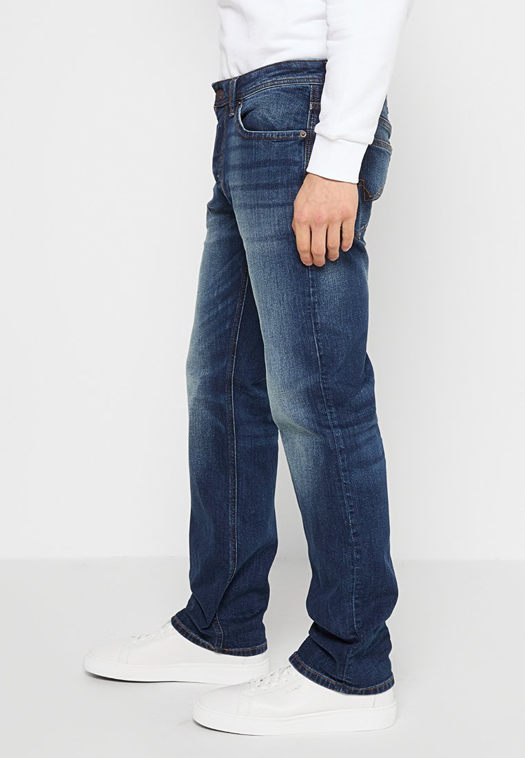 Jeans en denim de couleur bleu foncé avec une coupe droite, présentant une légère décoloration. Assortis à des chaussures blanches ; poches avant visibles.